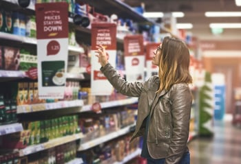 Shopper reaching towards a product in a shop on a high up shelf.