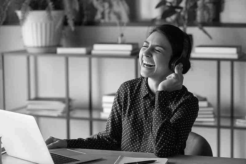 Woman laughing while wearing headphones and working on a laptop at a desk