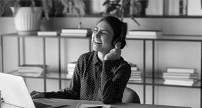 Woman laughing while wearing headphones and working on a laptop at a desk